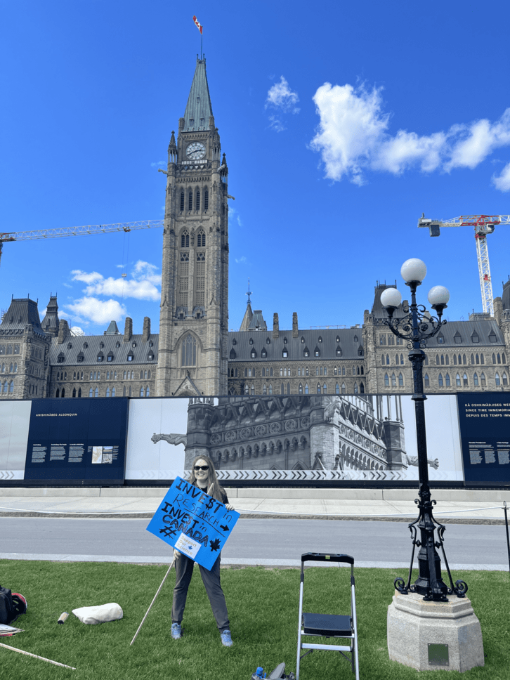 Pictured: Andrea Wishart holding Support Our Science protest sign in front of Parliament Hill