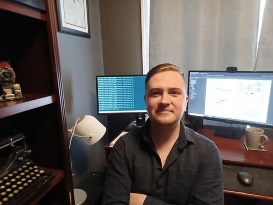 Josh Neudorf, PhD, posing for a photo in front of his computer desktop while conducting research