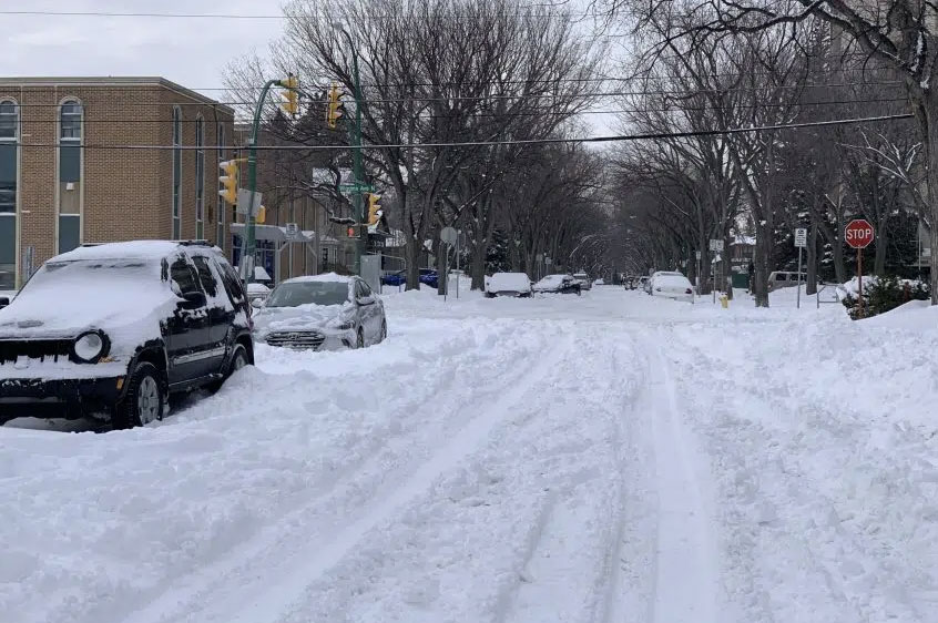 Image of Saskatoon street in the winter; snow is covering the road and there are two parked cars with snow